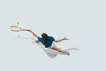 Zelfklevend Fotobehang Young woman in blue shirt playing tennis. She hits the ball with a racket. Indoor studio shot isolated on white. Youth, flexibility, power and energy. Negative space. Top view. © master1305