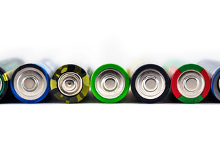Old AA batteries of different colors are stacked in a line. Batteries on white background