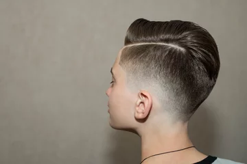  Stylish modern retro haircut side part with mid fade with parting of a school boy guy in a barbershop on a brown background © vika33