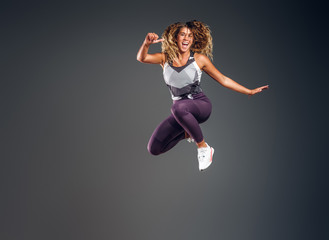 Cheerful happy woman is showing her performance at photo studio on the grey background.