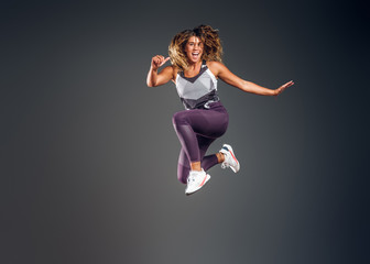 Cheerful happy woman is showing her performance at photo studio on the grey background.
