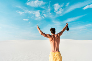 back view of sexy man holding glass and bottle on beach in Maldives