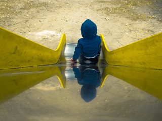 Little boy on children's slide with yellow sides and a shiny metal surface. Top down view of children's slide with playing kid