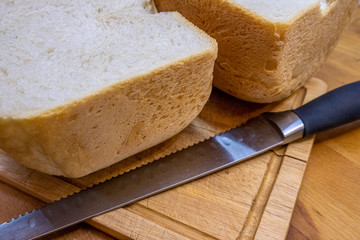 Freshly baked homemade bread cut in half on a wooden kitchen board and lying next to a bread knife for cutting bread.