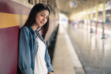 Naklejka na ściany i meble Portrait of an Asian woman smiling and leaning against the train at the train station. Tourism concept