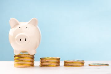 Cute piggy bank is climb a pile of gold coins on the white table with a blue background. savings money concept.