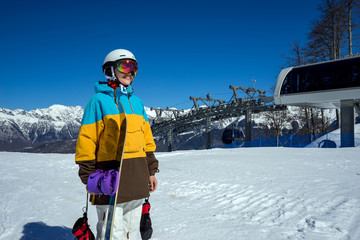 Fototapeta na wymiar Portrait of woman snowboarder on background of cableway and beautiful landscape of snowy high mountains Caucasus at Krasnaya Polyana, standing with snowboard