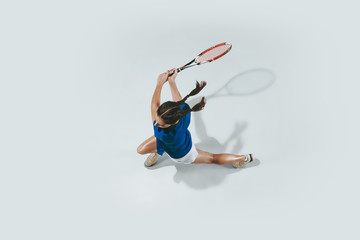 Young woman in blue shirt playing tennis. She hits the ball with a racket. Indoor studio shot...