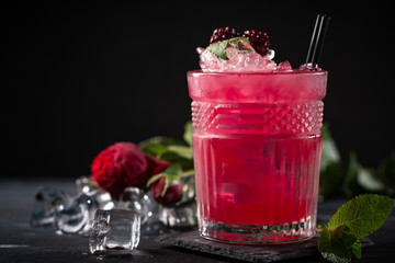 Alcoholic cocktail with blackberries, mint and ice on a dark wooden background. Refreshing red drink in a glass