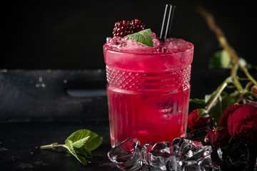 Alcoholic cocktail with blackberries, mint and ice on a dark wooden background. Refreshing red drink in a glass