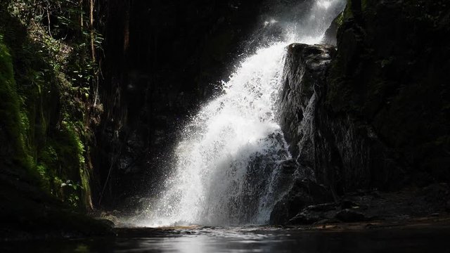 Slow motion of the sun shining on a rushing waterfall in the middle of the African jungle
