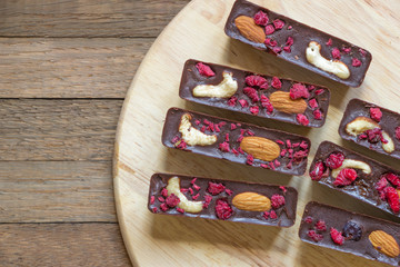 Delicious raw foods dessert from natural chocolate, cashew, almond and raspberry. Sweet sticks lay on round kitchen board on wooden background with copy space. Dietary tea treat. Healthy meal concept.