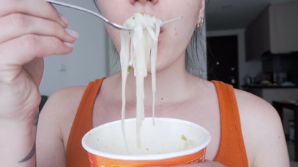 A woman in a red blouse is eating noodles with chopsticks. Close-up