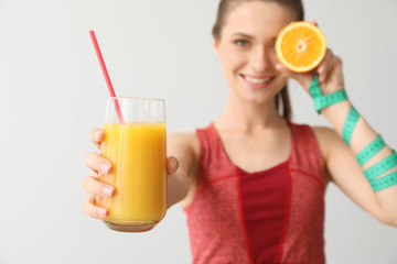 Sporty woman with measuring tape and healthy orange juice on light background. Diet concept