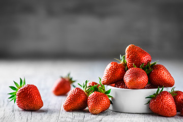 Fresh strawberries in white porcelain bowl on rustic table and grey background.
