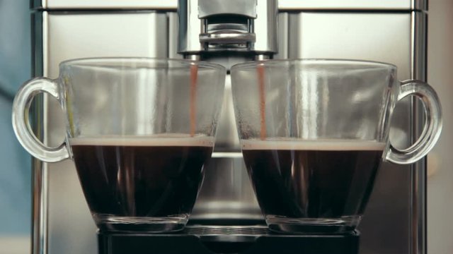 Preparation two natural delicious coffee simultaneously in the automatic coffee machine. Coffee is poured into cups. Good morning. 