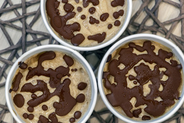 Close up raw fruit ice cream with natural chocolate droplets in a white paper cups on table covered with wicker tablecloth. Top view. Healthy vegan sweet dessert. Delicious harmless food.