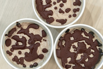 Sweet recipe of delicious harmless food. Close up raw fruit ice cream from bananas and coconut cream with natural chocolate droplets in a white paper cups on white wooden table. Top view