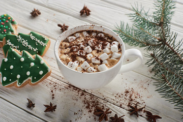 cacao with marshmallow in cup on white wooden table with fir branch and Christmas cookies