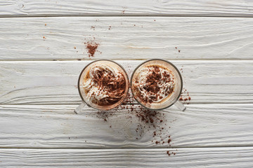 top view of cacao with whipped cream and cacao powder in mugs on white wooden table