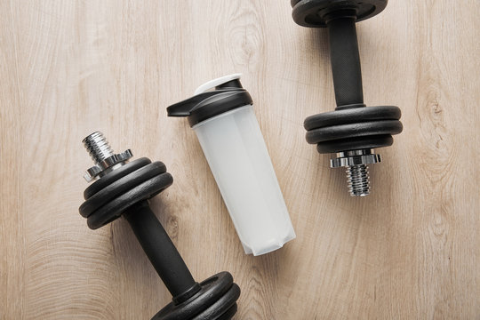 top view of sports bottle near heavy dumbbells on wooden surface
