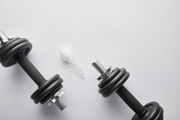 top view of spoon with protein powder near heavy dumbbells on white