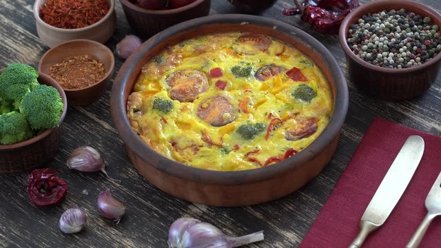 Ceramic bowl with vegetable frittata, simple vegetarian food. Frittata with egg, tomato, pepper, onion, broccoli and cheese on wooden table, close up. Italian egg omelette, rotates
