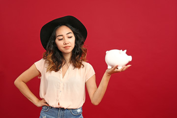 Asian woman with piggy bank on color background