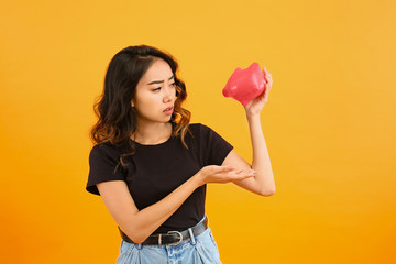 Sad Asian woman with empty piggy bank on color background