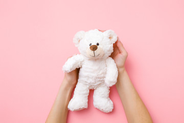 Smiling white teddy bear in girl hands on pastel pink background. Kids best friend. Point of view...