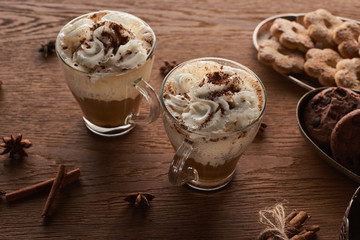 Christmas cacao with whipped cream on wooden table near spices and cookies