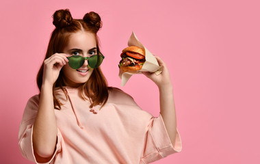 Beautiful teenage girl with red hair holding burger and beverage in hand. Ginger student girl has...