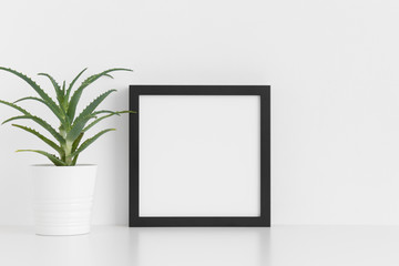 Black square frame mockup with a aloe vera in a pot on a white table.