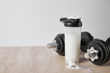 Obraz na płótnie Canvas spoon with protein powder near heavy dumbbells and sports bottle isolated on grey