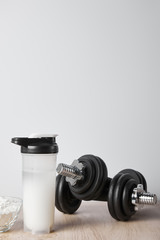 Obraz na płótnie Canvas sports bottle with protein shake near dumbbells isolated on grey