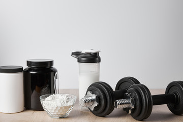 Obraz na płótnie Canvas protein shake in sports bottle near jars and dumbbells on white