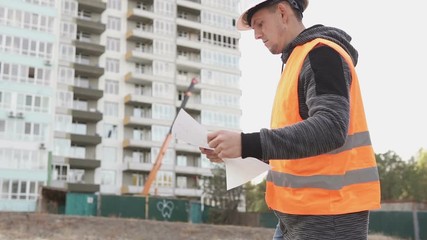 Young builder at a construction site walks with drawings