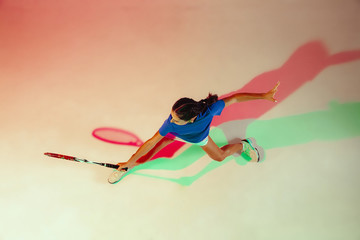 Young woman in blue shirt playing tennis. She hits the ball with a racket. Indoor studio shot with mixed light. Youth, flexibility, power and energy. Top view.
