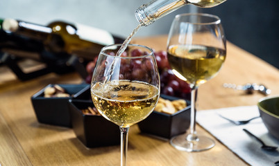 Pouring white wine into the glass against wooden table