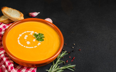 Pumpkin and carrot soup on black  stone background. Vegetarian soup in a rustic bowl with bread. Top view. Copy space.