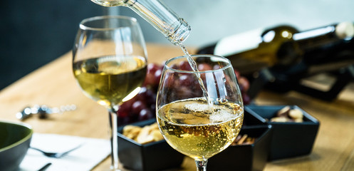 Pouring white wine into the glass against wooden table