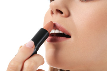 Beautiful young woman applying lipstick against white background, closeup