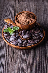 Whole dry cocoa beans in wooden bowl spoon mint on old rustic background with copyspace.