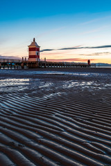 Sunrise over the sea. The lighthouse of Lignano Sabbiadoro and the games of sand and colors. Italy