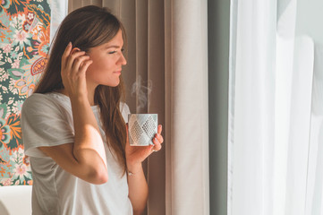 Woman with cup of hot drink by the window. Looking at window and drink tea. Good morning with tea. 