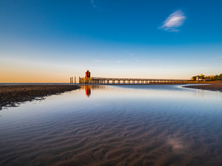 Fototapeta premium Sunrise over the sea. The lighthouse of Lignano Sabbiadoro and the games of sand and colors. Italy
