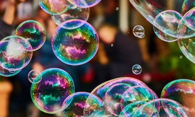 Metallic glowing colorful soap bubble in the air in front of a blurry abstract background - obrazy, fototapety, plakaty