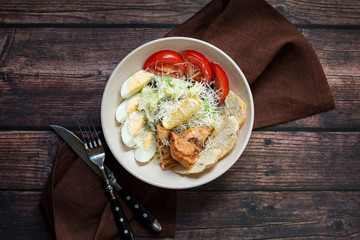 Grilled salmon caesar salad with dressing on dark rustic wooden table