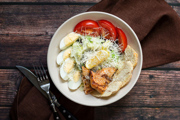 Grilled salmon caesar salad with dressing on dark rustic wooden table