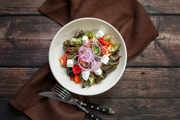 Greek salad with red onions, feta cheese, cherry tomatoes and olives on dark wooden table